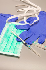 Health, protection,treatment and medical concept: Medical syringe with needles, mask and medical gloves on gray background.