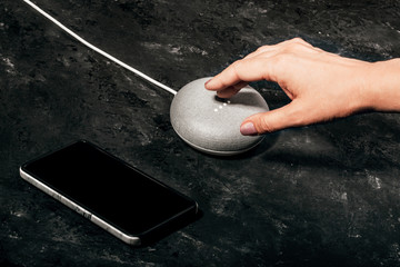Digital Assistant concept. Women's hand touches smart speaker with LED lights activated on concrete...