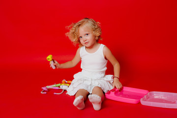 Adorable smiling little girl playing with toy syringe isolated on red. Child dream to be a doctor
