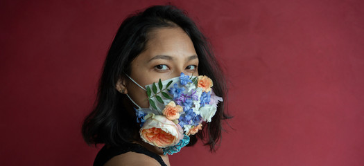 Woman in protective medical mask with flowers on red background.