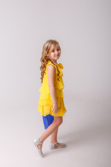 a little girl in a yellow dress with a shopping bag dancing on a gray background