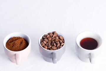 Three cups of different condition of coffee - beans, freshly ground and coffee drink on a marble light grey background.