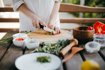 Woman's hands chopping green onions on a wooden plate. Making guacamole
