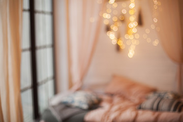 Blurred background of a cozy room with a bed and a chandelier.