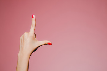 Woman's hands with bright manicure isolated on pink background L letter