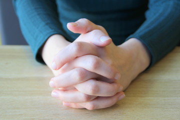 Palms folded in prayer. Clasped fingers. Girl sits and holds hands in front of her hands clasped together
