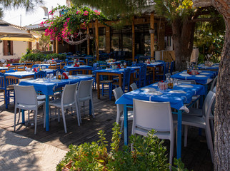 Traditional greek tavern with tables served and prepared for lunch of tourists in the summer season in Kastos island, Lefkada Regional unit, Ionian Islands, Greece.