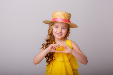 a little girl in a straw hat smiles on a gray background