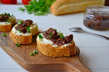 French baguette with cream cheese and dried tomatoes on a white background.