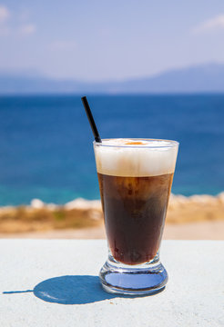 Glass of yummy iced coffee or greek freddo cappuccino on the seascape background on a summer sunny day in Kastos island, Lefkada Regional unit, Ionian Islands, Greece.