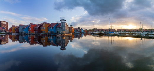 Fototapeta premium Panorama of Groningen harbor in Holland at sunrise. In the harbor there are boats and in the blue sky white clouds over colorful houses.