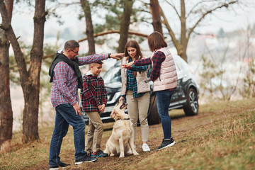 Fototapeta premium Happy family have fun with their active dog near modern car outdoors in forest