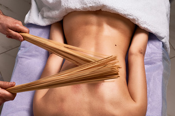 Male masseur doing Japanese massage with bamboo sticks on beautiful naked woman body in the spa...