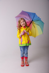 baby girl with bright umbrellas in boots on a gray background, spring