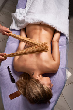 Male masseur doing Japanese massage with bamboo sticks on beautiful naked woman body in the spa salon. Beauty treatment concept.