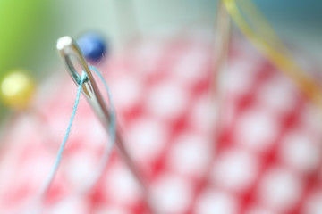 Needle eye with piece of blue thread stick out of pincushion