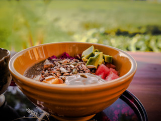 close-up of vegan fruit smoothie bowl with wooden spoon, granola, chia, seeds, mango, dragon fruit, watermelon, avocado for healthy breakfast with green grass in background