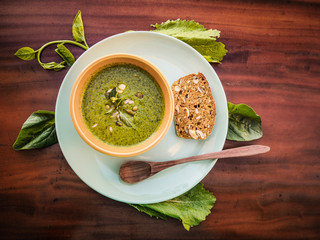 top view of a healthy vegan green soup with pumpkin and sunflower seeds, bread, salad and wooden spoon in a bowl on a plate on table