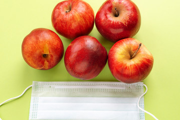 Juicy apples lie on a green background , next to a protective medical mask. Fruit from China, a concept for protecting the population during a virus pandemic COVID-19, copy space
