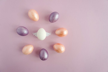 A white Easter egg with wings is surrounded by colorful eggs. The concept of inspiration and leadership. Copy space for text.