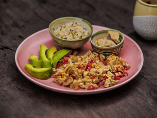 close-up of vegan scrambled tofu with bell pepper, mushrooms, avocado, quinoa and spread on a plate on table for a healthy breakfast