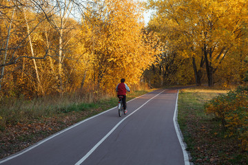 Retired woman riding a bike in bright autumn park