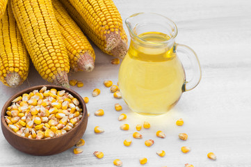 Corn oil in glass bottle with dried corn groats and kernels on rustic backdrop. Cooking oil composition