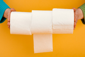 A roll of toilet paper in a woman's hand on a yellow background