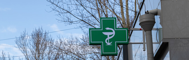 Urban pharmacy or drug store sign, led display green cross on the wall in the city street, copy space.