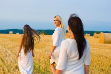 horizontal photo of two beautiful sisters and their mother in white dresses against the sky and field