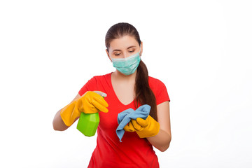 Young woman in mask and gloves holds spray bottle and rag isolated on a white background. Cleaning the house and premises, the prevention of viral diseases.