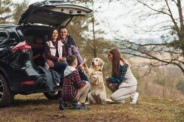 Happy family have fun with their dog near modern car outdoors in forest