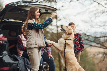 Happy family have fun with their dog near modern car outdoors in forest