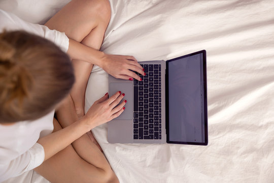 Frau mit Laptop auf dem Bett sitzend