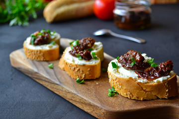 French baguette with cream cheese and dried tomatoes on a dark background.