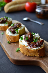French baguette with cream cheese and dried tomatoes on a dark background.