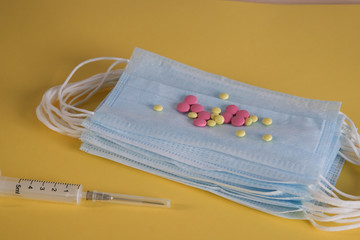 Blue medical disposable mask on a yellow background. Multicolored round tablets. A medical syringe. Insulations