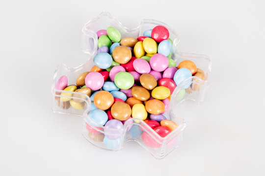 Many multicolored glazed chocolate candies in plastic box candy container in white background