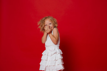 Pretty little blonde curly girl in white dress laughing isolated on red