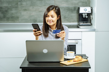 Smiling woman online shopping using a smartphone laptop and credit card at home