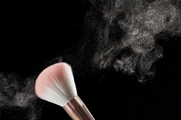 Make-up brush with powder on it and heap of powder on black background. Photo with copy space.