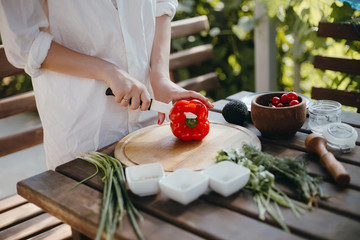 Woman's hands cutting red pepper on wooden plate. Healthy vegetarian food