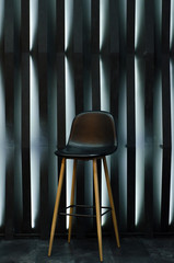Black leather bar stool with wooden legs stands in interior against background of wall with boards...