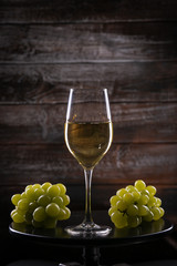White wine glass with grapes on a table on a wooden background