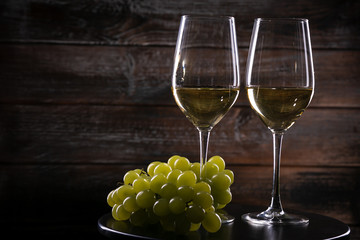 Two full white wine glasses with grapes on a table on a wooden background