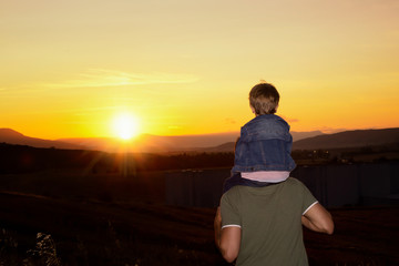 Boy climbed on his father's shoulders looking the sunset