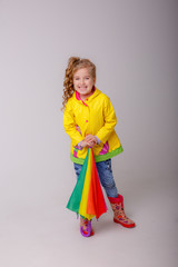 baby girl with bright umbrellas in boots on a gray background, spring