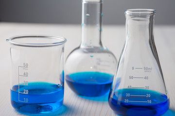Close-up of three glass test tubes with blue liquid, on white wooden table and gray background, horizontal