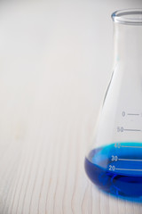 Close-up of half glass test tube with blue liquid, on defocused white wooden table, vertical with copy space