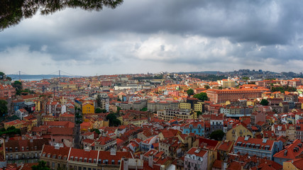 A big panorama of lisbon from a terrace. All the rooftops from above and the 25 de Abril bridge at the back.